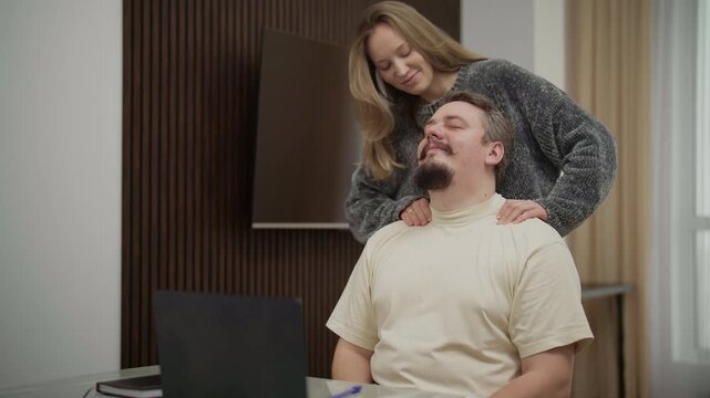 Caring woman massaging her husband's shoulders at home office