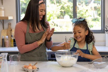 Fototapeta premium Mother and child baking at marble counter in kitchen whisking batter in glass bowl wearing aprons