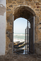 Obraz premium Atlantic Ocean and a rocky coastline seen through a gate in the city walls of the fortified city of Asilah, Morocco