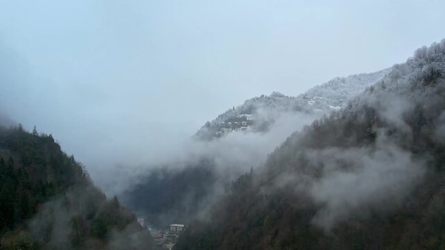 Aerial view of misty mountains and snowy forests covering a dramatic valley landscape in Rize, Turkey. Scenic winter nature in the Black Sea region with fog drifting through forested hills.