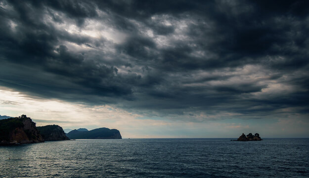 Dramatic storm clouds over the Adriatic Sea coast in Petrovac Montenegro with dark moody sky and distant rocky islands.