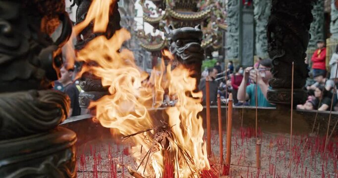 New Taipei City, Taiwan, May 12, 2025: The blazing flames of incense burners in a traditional temple create a dynamic contrast with the crowds of people praying and the magnificent dragon pillar carvi