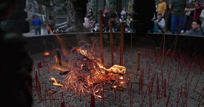 New Taipei City, Taiwan, May 12, 2025: The blazing flames of incense burners in a traditional temple create a dynamic contrast with the crowds of people praying and the magnificent dragon pillar carvi