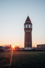 Fototapeta premium Historic Water Tower at Golden Sunrise, Industrial Landmark Silhouette against a Vibrant Summer Sky
