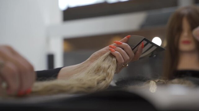 Close up of a hair stylist's hands with bright orange nails holding a bundle of blonde hair extensions during a professional consultation