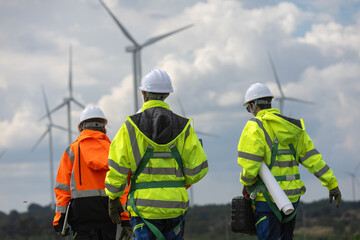 Engineer wind turbine technicians walking through renewable energy wind farm inspecting equipment, discussing maintenance plan. Teamwork in sustainable electricity industry, clean power technology.