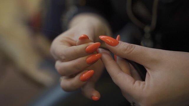 Close up of a stylist's hands with bright orange nails rolling a keratin bond onto a hair extension strand