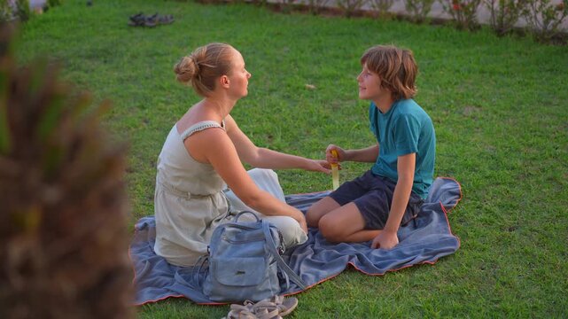Young mom spending quality time with her two sons in a lush green park, enjoying nature, laughter, and joyful family bonding moments outdoors.