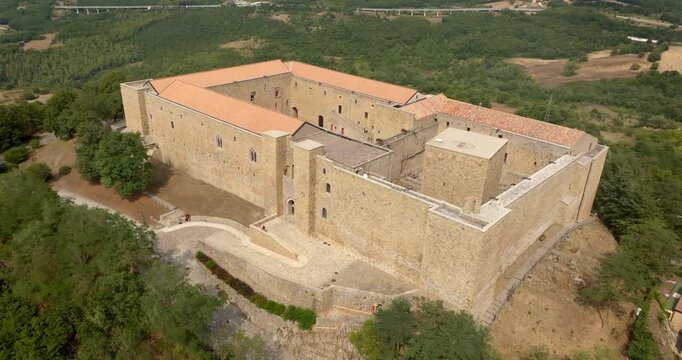 Aerial view of the entrance to Lagopesole Castle, located in Basilicata, Italy. It is a medieval castle dating back to the time of Frederick II. The fort sits atop a hill overlooking a vast landscape.