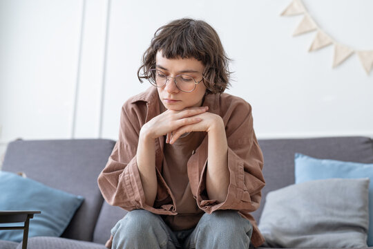 Depressed teen girl sadly sits on sofa at home. Nervous schoolgirl feeling frustration hiding from society in loneliness. Upset unhappy teenager has awkward age problems, misunderstanding with parents