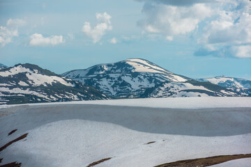 Scenic alpine landscape with sunlit snowfield with snow cornice above abyss against large snow-capped rock mountain top. Sunlight and shadows on snowy field near rocky precipice edge in high mountains © Daniil