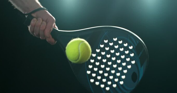 Super slow motion close-up of a hand holding a padel racket as a yellow ball hits the surface, filmed at 1000 fps. Dramatic studio lighting highlights the impact, motion of the racket and ball.