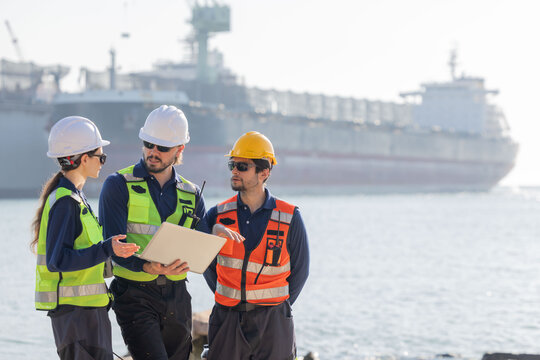 Workers discuss plans at a port with a cargo ship in the background