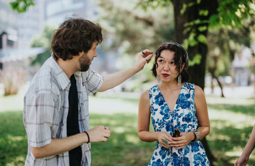 Obraz premium Two friends in a sunny park share a candid moment. A man adjusts a womans hair while they converse.