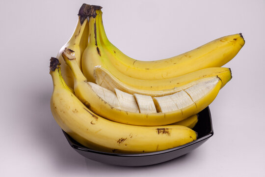 Bunch of ripe yellow bananas in black bowl, one partially pilled and cut in to slices