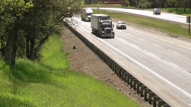 Three oncoming trucks passing on California rural freeway with truck appearing in opposite lanes, in background.