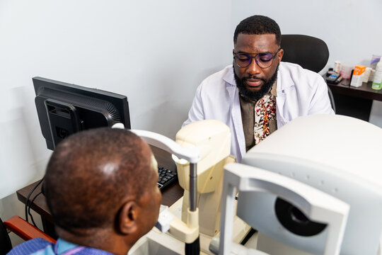 Optometrist examining a senior African man's eyes in a clinic with a non-contact tonometer (NCT)