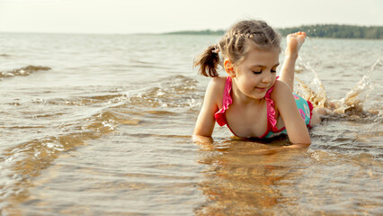 Fototapeta premium Happy little girl playing in shallow lake water on summer day