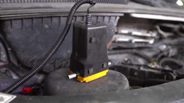 A car part sits on the engine block under the hood of a vehicle. Wires are connected to the part while tools and other components are nearby. This scene shows work in a garage.