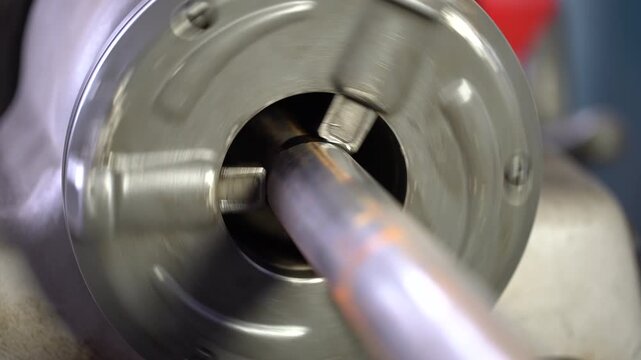 A lathe chuck holds a workpiece while it rotates at low speed. This action produces a steady ringing sound and slight vibrations in the workshop environment.