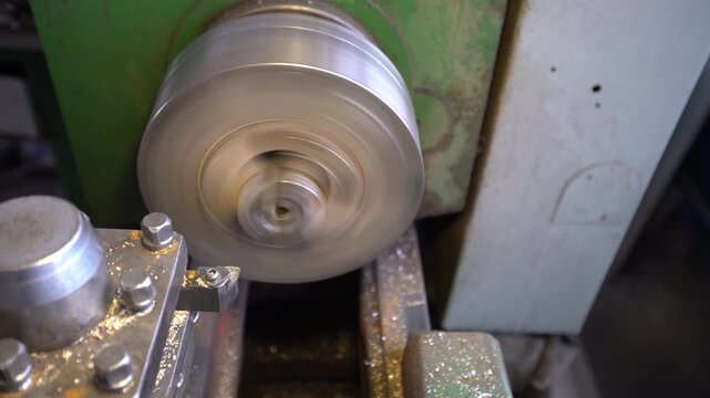 Lathe chuck turns steadily in a workshop. The machine creates a mechanical hum and metallic sounds while shaping metal. Tools are positioned, showcasing the process of machining.