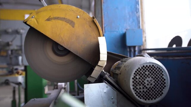 A cutoff disc machine operates in a factory, spinning a metal disc. It produces a steady metallic sound as it cuts through materials. The machine runs efficiently, showing signs of use and purpose.
