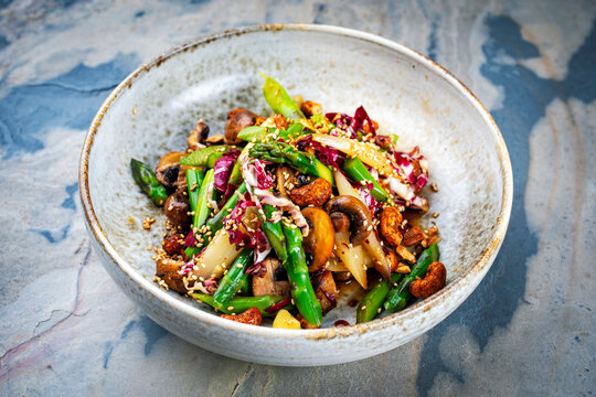 Cold vegetarian salad with green and white asparagus tips, radicchio, roasted spicy cashew nuts and sesam served as close-up in a design bowl