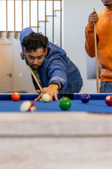 Diverse males lining up pool shot at blue felt table in home with cues, billiard balls