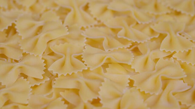 Foamy beige farfalle arranged artistically. Closeup of dry bowshaped pasta with warm hues. Detailed image of uncooked farfalle in uniform pattern on warm background