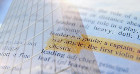 Naklejka premium Showing highlighted dictionary entry 'leader' reflecting skyscraper facade over desk surface
