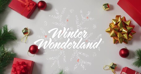 Surrounding centered white Winter Wonderland with dotted snowflake on table, red boxes, gold bow