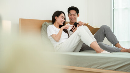 Couple Sitting on Bed Enjoying Time Together With a Phone and Book in a Bright Room