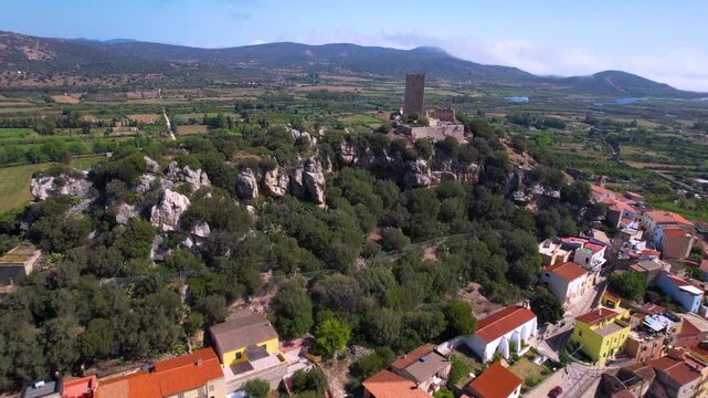 Sardinia Posada aerial flight towards medieval tower over colorful houses to green fields Italy drone cinematic footage 4k Castello della Fava hilltop village travel destination scenery