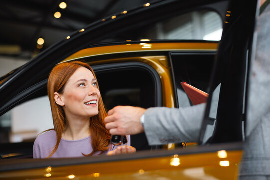 Woman receiving car key from salesman while sitting in vehicle at dealership