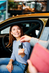 Woman receiving car keys from salesman while sitting in new car at dealership