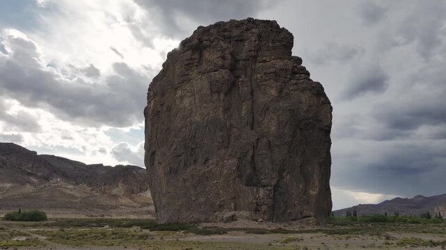 wide aerial orbit shot of the immense and colossal Piedra Parada rock formation under a cloudy sky in Chubut, Patagonia, Argentina