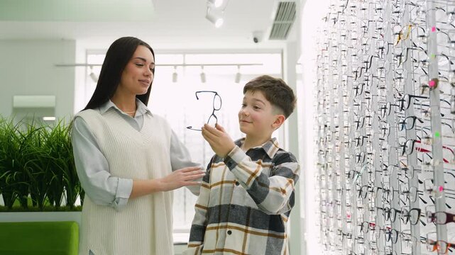 Mother helping her son choose new eyeglasses in an optical store