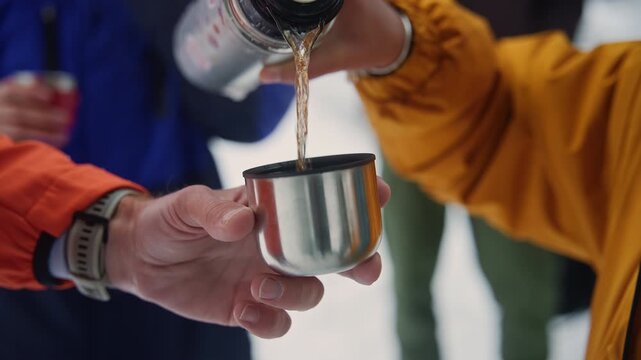 Person pouring hot tea from thermos in winter