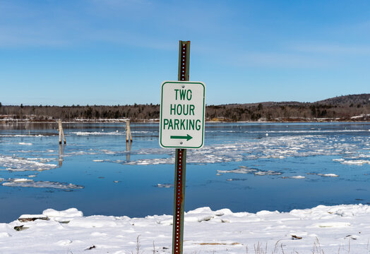 View of a two hour parking sign in the winter with a bay with wood pilings in the background.