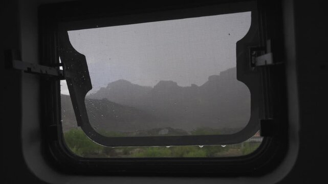 Rain drops falling over an open camper van window with a silhouette of mountains in the background