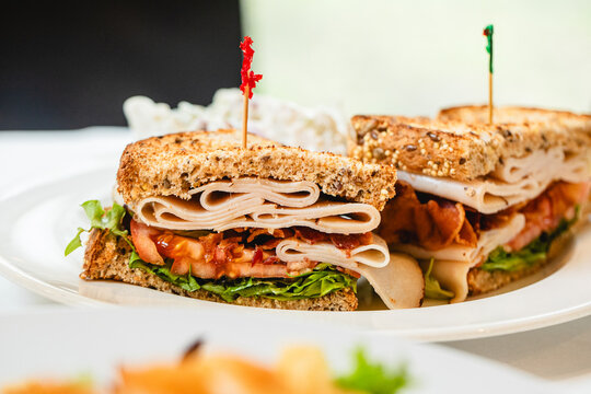 A turkey BLT sandwich served on a white plate in a modern bright restaurant and cafe 