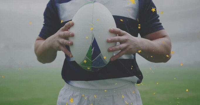 Rugby player adjusting grip, lifting ball to chest on misty sports pitch, golden stars showing pass