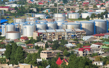 Obraz premium Industrial oil tanks stand near residential houses. Silver reservoirs and terminal infrastructure during global oil market crisis. Strategic energy supply concept image