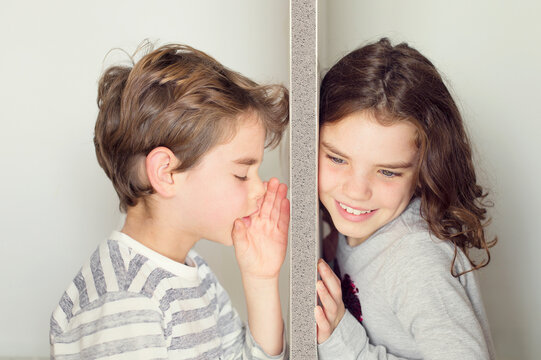Close-up side view of a Boy standing on one side of a wall whispering a secret to a girl listening on the other side of a wall