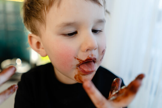 A three year old child with melted chocolate on face. Close up view highlighting messy skin and expression. Concept of forbidden treat, unhealthy diet, allergies, diabetes risk.