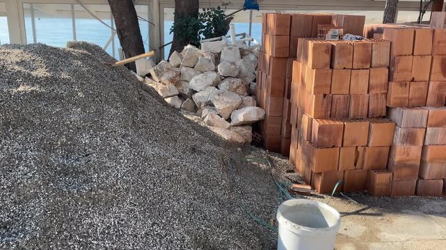 Construction site with gravel pile, rocks, and stacked bricks suggesting architectural work