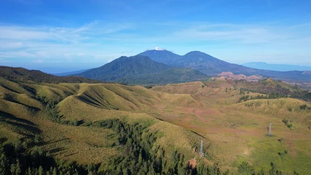 Aerial drone footage of the Kawah Wurung dry valley, at sunrise, with some forests, and Raung volcano mountains in the background, in Bondowoso regency, Java island, Indonesia