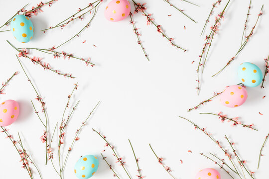 Easter flat lay with pastel pink and blue polka dot eggs and delicate ginestra branches on a white background. Minimalist spring composition with copy space, perfect for holiday cards and branding