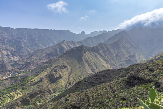 Un espectacular paisaje de crestas volc&aacute;nicas afiladas donde las nubes se desploman sobre las cumbres, creando un juego de luces y sombras sobre la vegetaci&oacute;n de tuneras y matorral.