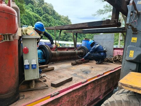 Industrial workers using a forklift and webbing slings to carefully lift a tripper conveyor axle for maintenance. 